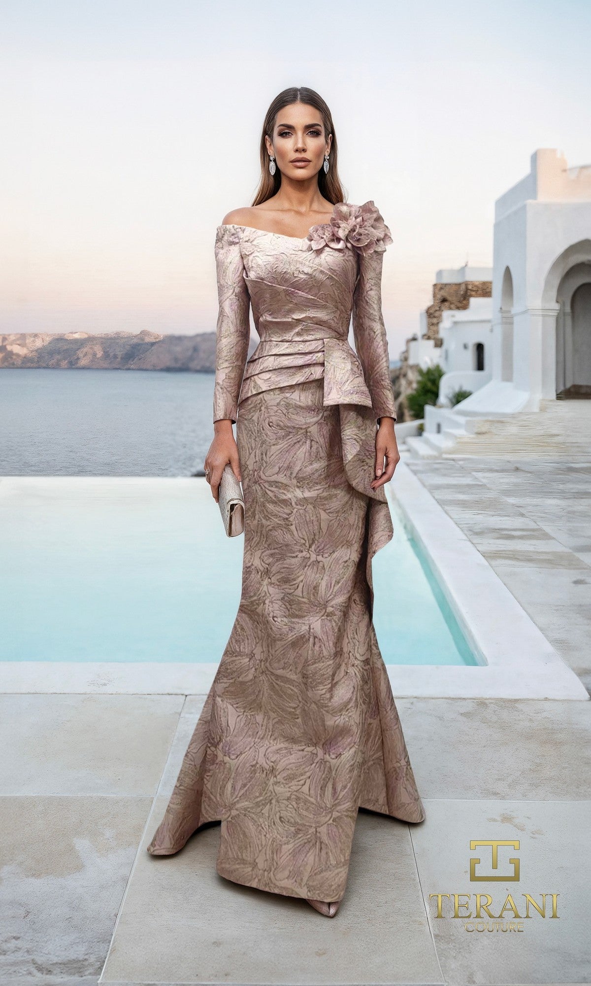 A woman in a sophisticated blush rose Terani 261M6448 long formal dress stands by a pool overlooking the sea, framed by white Mediterranean-style architecture in the background.